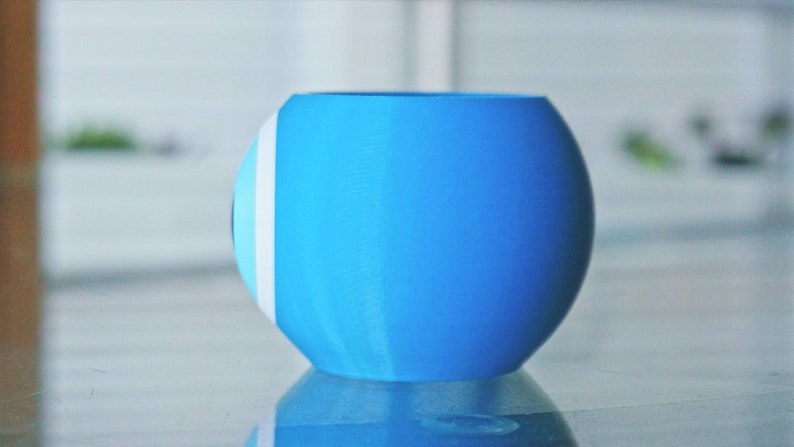 May include: A light blue ceramic planter with a white and light blue design. The planter is round and has a smooth surface.