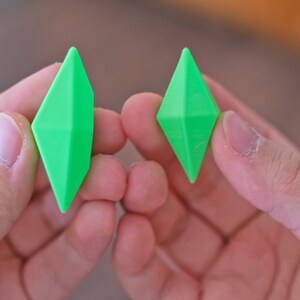 May include: Two bright green diamond-shaped objects are held in the hands of a person. The objects are made of a smooth, shiny material.