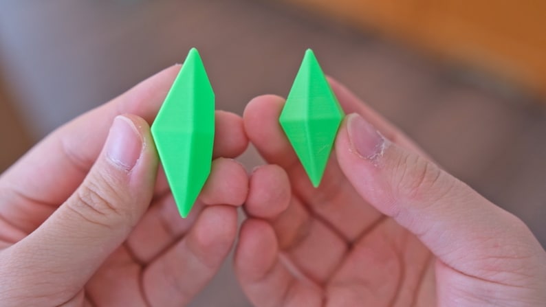 May include: Two bright green diamond-shaped objects are held in the hands of a person. The objects are made of a smooth, shiny material.