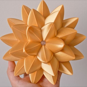 May include: A gold-colored, geometric, 3D printed flower with a starburst design. The flower is made of many small, overlapping petals.
