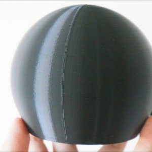 May include: A dark gray sphere with a lighter gray stripe running vertically down the side.
