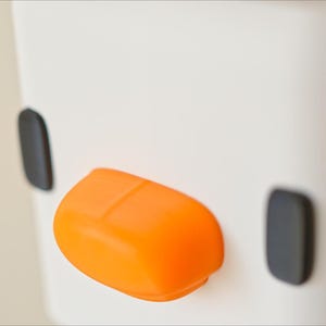 Pu&ograve; includere: Un oggetto in ceramica bianca con un design nero e arancione. L'oggetto ha due cerchi neri e un becco arancione arrotondato.