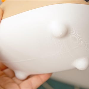 May include: White ceramic planter with a textured bottom and four small feet. The planter has a rounded shape and a smooth, white finish.
