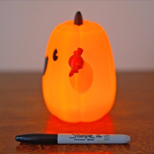 May include: Orange pumpkin-shaped Halloween decoration with a black face and red candy corn. The pumpkin is lit from within, giving it a warm glow.