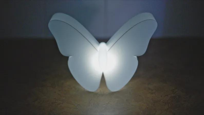 May include: A white, butterfly-shaped light fixture with a bright, glowing center. The wings are curved and symmetrical, and the fixture is set against a dark background. The light is soft and diffused.