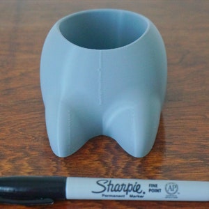 May include: A light blue ceramic planter shaped like a cartoon animal with two small feet. The planter is about 4 inches tall and 3 inches wide. A black Sharpie marker is in the foreground for scale.