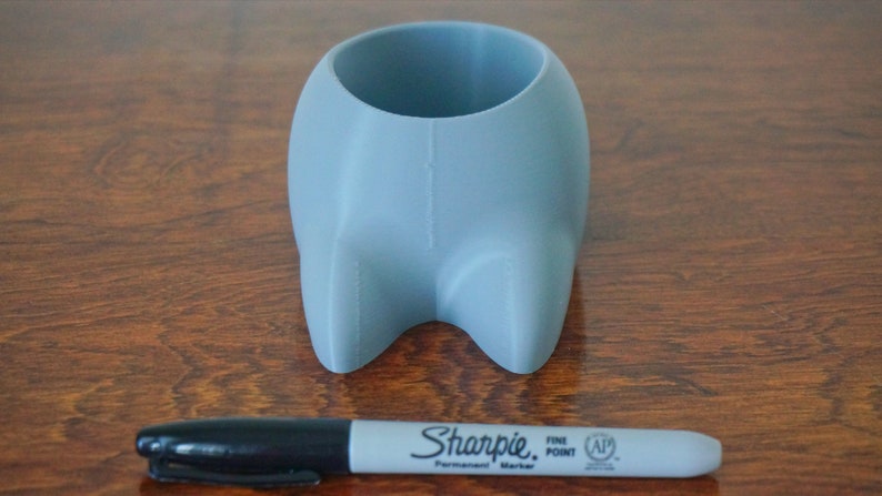 May include: A light blue ceramic planter shaped like a cartoon animal with two small feet. The planter is about 4 inches tall and 3 inches wide. A black Sharpie marker is in the foreground for scale.