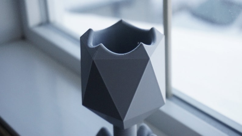 May include: A gray geometric planter with a unique, angular design. The planter is made of a smooth, matte material and has a wide opening at the top.