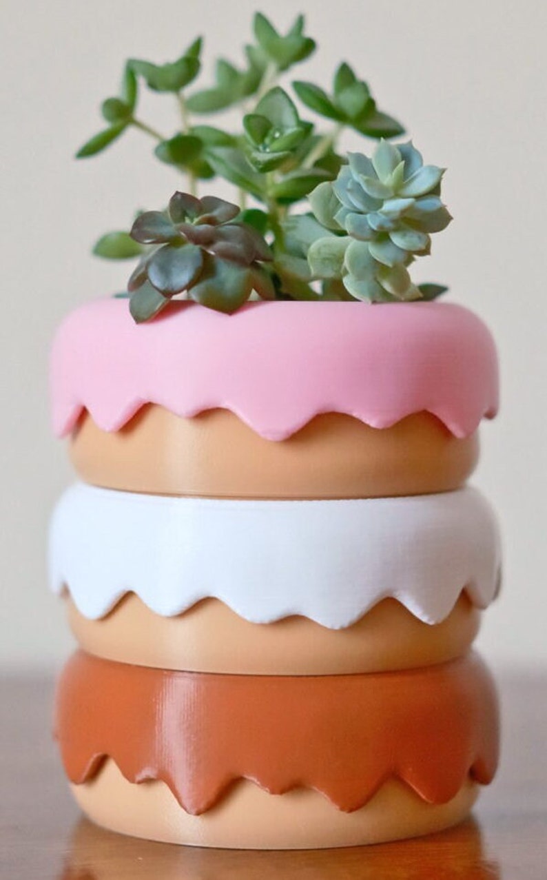 Puede incluir: Un conjunto de tres macetas de cer&aacute;mica en rosa, blanco y naranja con un borde festoneado. Las macetas est&aacute;n llenas de una variedad de suculentas verdes.