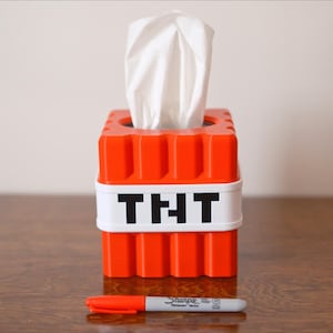 K&ouml;nnte beinhalten: Orangener Taschentuchspender in Form eines Minecraft TNT-Blocks mit einer wei&szlig;en Taschentuchbox im Inneren und dem Wort "TNT" auf der Vorderseite.