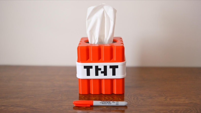 K&ouml;nnte beinhalten: Orangener Taschentuchspender in Form eines Minecraft TNT-Blocks mit einer wei&szlig;en Taschentuchbox im Inneren und dem Wort "TNT" auf der Vorderseite.
