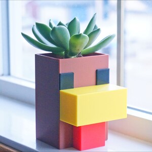 K&ouml;nnte beinhalten: Ein brauner, gelber und roter Pflanzer in Form eines Minecraft-Huhns, mit einer gr&uuml;nen Sukkulente, die darin w&auml;chst.