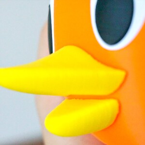 May include: Close-up of a bright orange and yellow rubber duck toy. The duck has a large, round black eye and a yellow beak.
