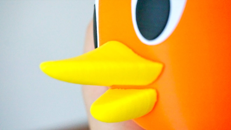 May include: Close-up of a bright orange and yellow rubber duck toy. The duck has a large, round black eye and a yellow beak.