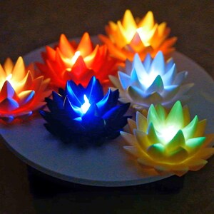 May include: Six lotus-shaped LED lights in different colors, including orange, yellow, white, blue, and green, arranged in a circle on a white surface.