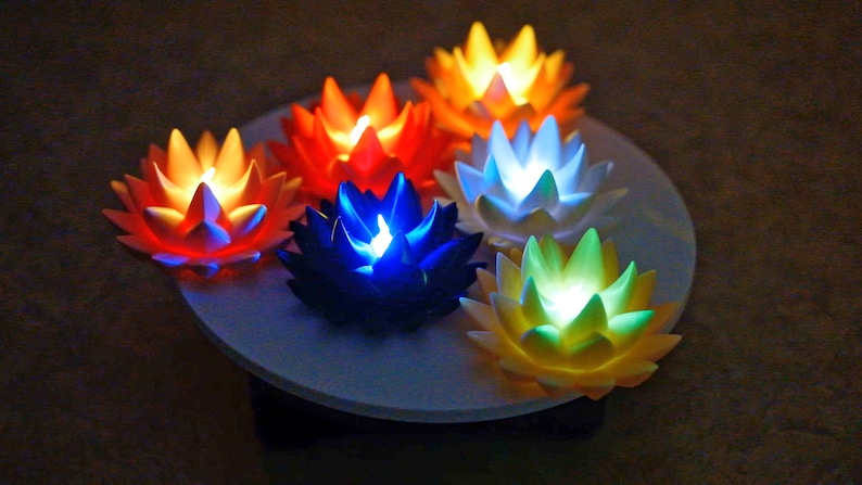 May include: Six lotus-shaped LED lights in different colors, including orange, yellow, white, blue, and green, arranged in a circle on a white surface.