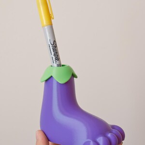 May include: Purple eggplant-shaped pen holder with a green top and a yellow Sharpie marker inside.
