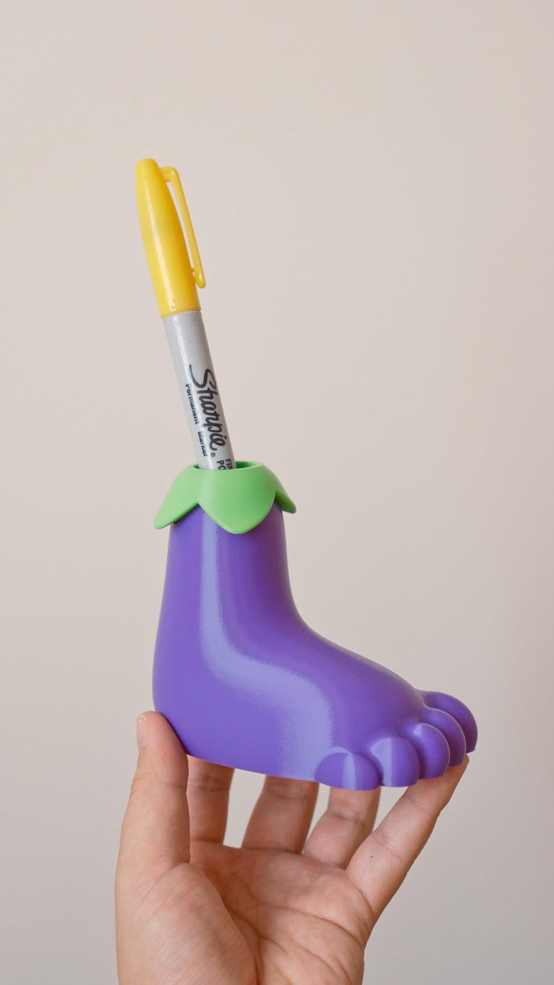 May include: Purple eggplant-shaped pen holder with a green top and a yellow Sharpie marker inside.