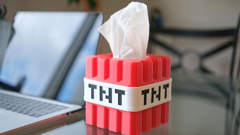 K&ouml;nnte beinhalten: Rote Plastik-Tischbox in Form eines Minecraft TNT-Blocks mit einem wei&szlig;en Etikett, auf dem auf jeder Seite "THT" steht.