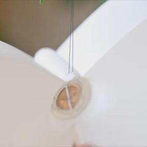 May include: A white paper butterfly with a circular, transparent center. The butterfly is suspended by thin, dark strings, suggesting it may be a mobile or decorative element. The wings are large and smooth.