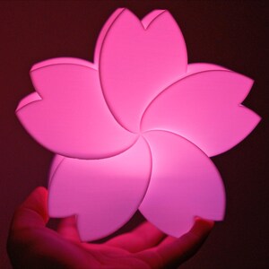 May include: A pink, plastic flower-shaped night light. The light is illuminated and has a soft glow.