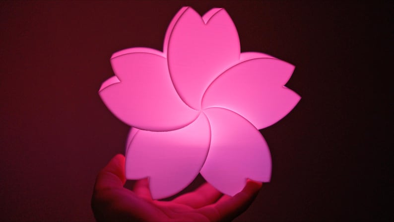 May include: A pink, plastic flower-shaped night light. The light is illuminated and has a soft glow.