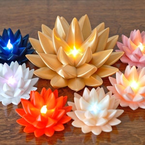 May include: Seven lotus-shaped candles with LED lights. The candles are in various colors, including gold, pink, white, blue, and orange. The candles are arranged in a circle on a wooden surface.