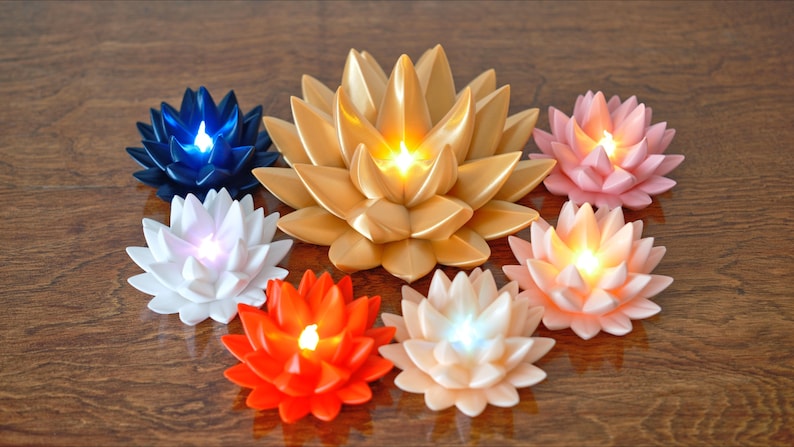 May include: Seven lotus-shaped candles with LED lights. The candles are in various colors, including gold, pink, white, blue, and orange. The candles are arranged in a circle on a wooden surface.