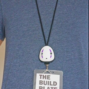 May include: A black lanyard with a white and purple No-Face character badge reel. Below the badge reel is a clear plastic card holder with the text "THE BUILD PLATE" and two keys.