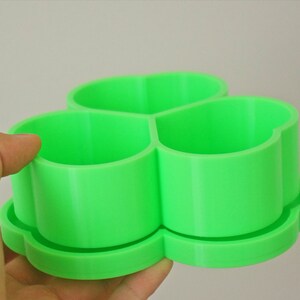 May include: A bright green, three-sectioned container with a clover-shaped base. The container is made of a smooth, solid material and is designed to hold small items. The design is simple and modern, suitable for various uses.