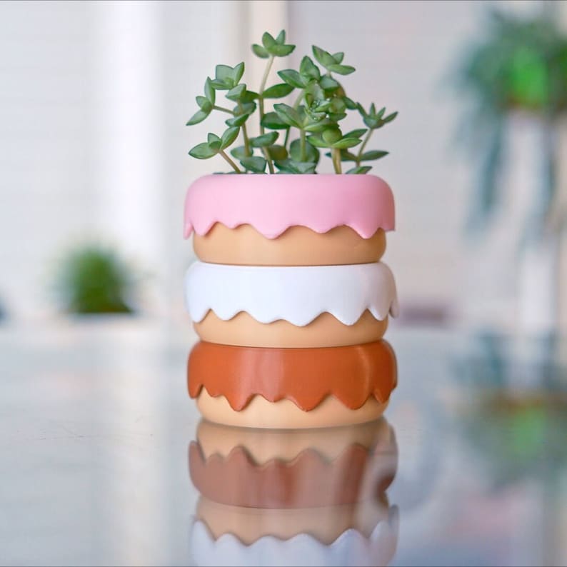 Puede incluir: Un macetero de tres niveles hecho de cer&aacute;mica con un esmalte rosa, blanco y marr&oacute;n. El macetero est&aacute; decorado con un borde festoneado y presenta una planta suculenta.