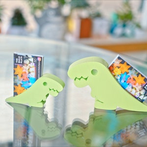 May include: Two green dinosaur-shaped card holders, each holding a business card with the text "The Build Plate".