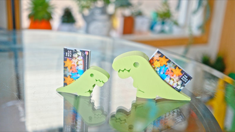 May include: Two green dinosaur-shaped card holders, each holding a business card with the text "The Build Plate".