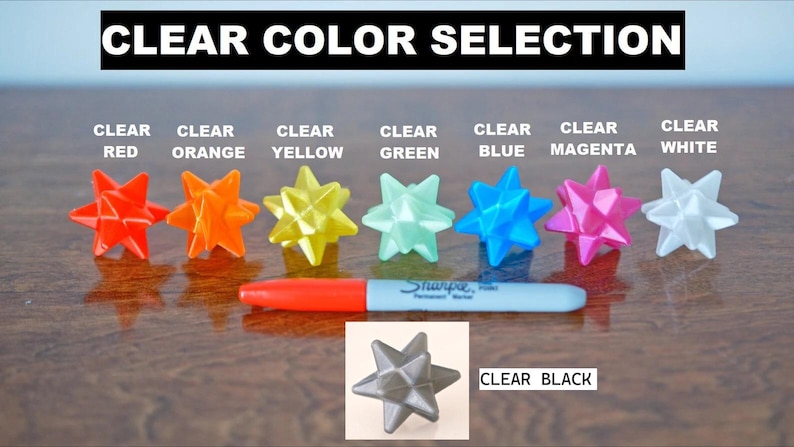 May include: Image showing a selection of clear, star-shaped ornaments in various colors: red, orange, yellow, green, blue, magenta, and white. A black Sharpie marker is in the center. The text "CLEAR COLOR SELECTION" is at the top.