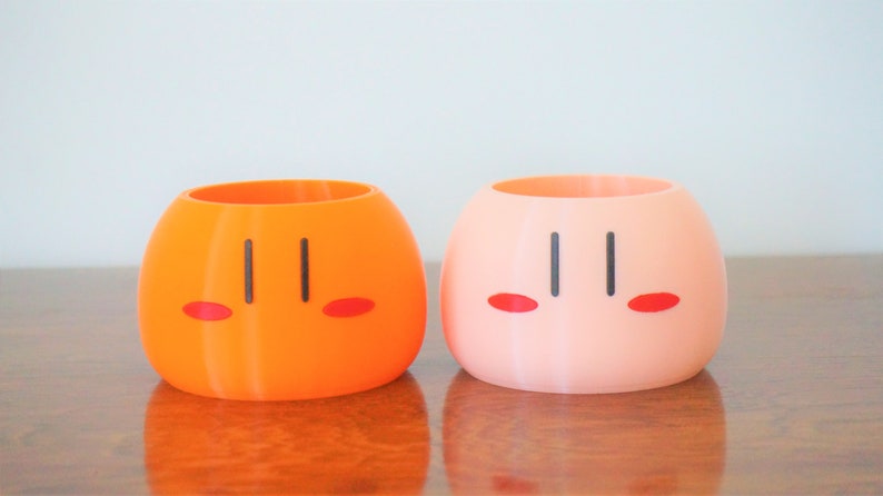 May include: Two ceramic dango-shaped planters, one orange and one pink, with black eyes and red cheeks.