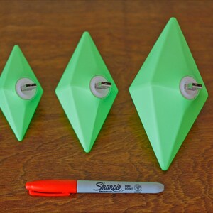 May include: Three green diamond-shaped USB drives of different sizes on a wooden surface. A red and white marker is in the foreground.