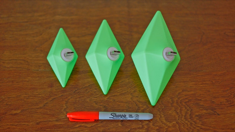 May include: Three green diamond-shaped USB drives of different sizes on a wooden surface. A red and white marker is in the foreground.