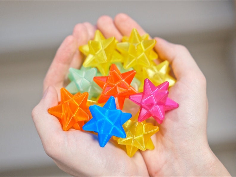 May include: A collection of colorful, star-shaped, plastic toys in a person's hands. The stars are in shades of yellow, green, orange, blue, and pink.