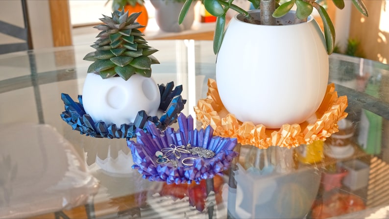 May include: Three white ceramic planters with different coloured crystal-like bases. The bases are blue, orange, and purple. The purple base has a few small pieces of jewellery inside.