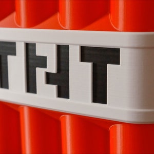 May include: A red and white block with the word "TNT" printed on it. The block is made of plastic and has a textured surface.