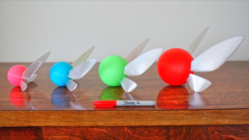 May include: Four different sized, round, hollow, plastic spheres with white wings attached to each. The spheres are pink, blue, green, and red. A white marker is in front of the spheres.