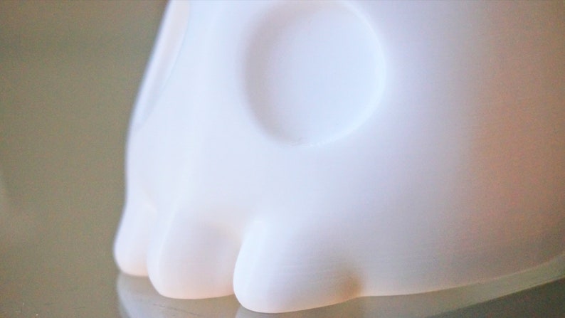 May include: White ceramic sculpture of a skull with a smooth, rounded surface. The skull has two large eye sockets and a prominent nose.