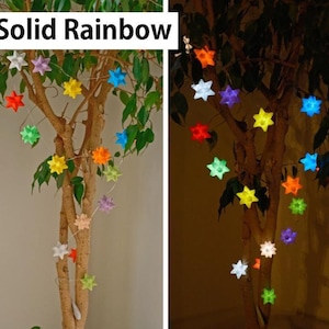 May include: A string of star-shaped lights in various colors, including red, yellow, green, and blue, are strung on a tree. The text "Solid Rainbow" is displayed at the top. The lights are illuminated, creating a festive and colorful display.