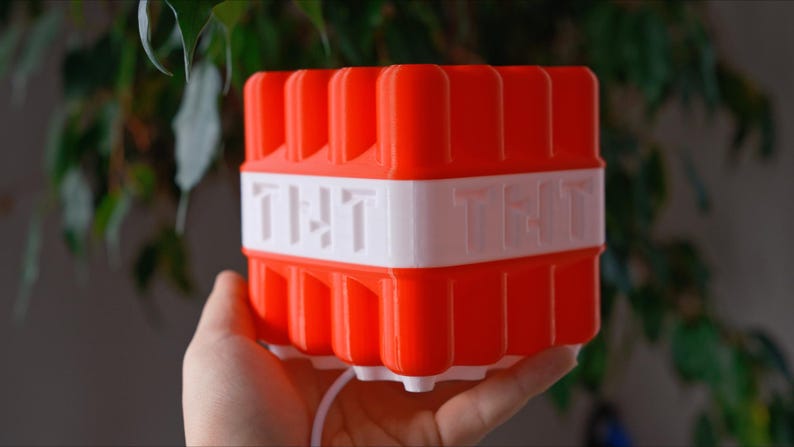 May include: A red and white plastic block with the word "TNT" printed on each side. The block is shaped like a cube and has a textured surface.