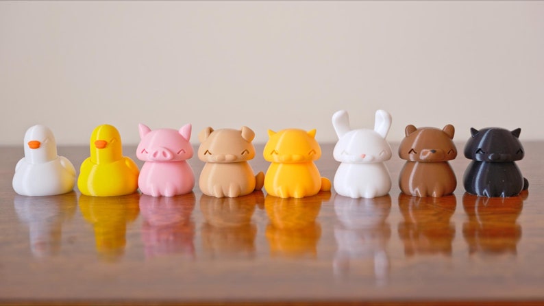 Peut inclure: Un ensemble de neuf figurines d'animaux imprim&eacute;es en 3D. Les figurines sont de diff&eacute;rentes couleurs, notamment le blanc, le jaune, le rose, le marron, l'orange et le noir. Les animaux comprennent un canard, un cochon, un ours, un chat, un lapin et un oiseau.
