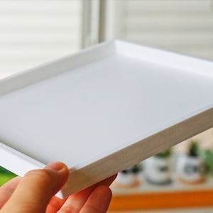 May include: A white rectangular tray with a raised edge. The tray is made of a smooth, white material and has a slightly textured surface.