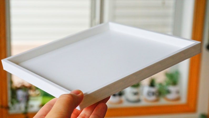 May include: A white rectangular tray with a raised edge. The tray is made of a smooth, white material and has a slightly textured surface.