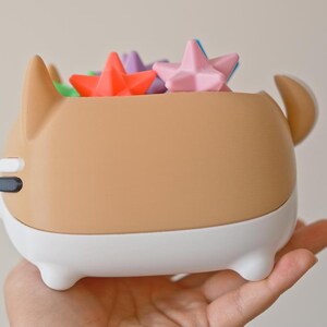 May include: A brown and white ceramic dog-shaped planter with a white rim. The planter is filled with colorful star-shaped objects.