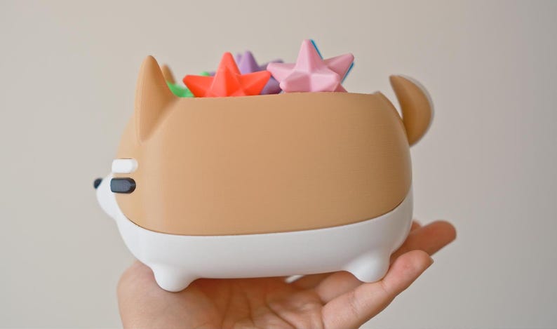 May include: A brown and white ceramic dog-shaped planter with a white rim. The planter is filled with colorful star-shaped objects.