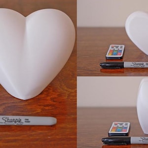 May include: Three white heart-shaped lamps with a remote control and a black Sharpie marker. The lamps are made of a smooth, white material and have a soft, rounded shape.